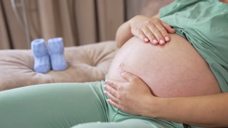 pregnant woman laying at the bed and relaxing at home with small baby shoes at the background. small shoes for the unborn baby. maternity prenatal care and woman pregnancy concept