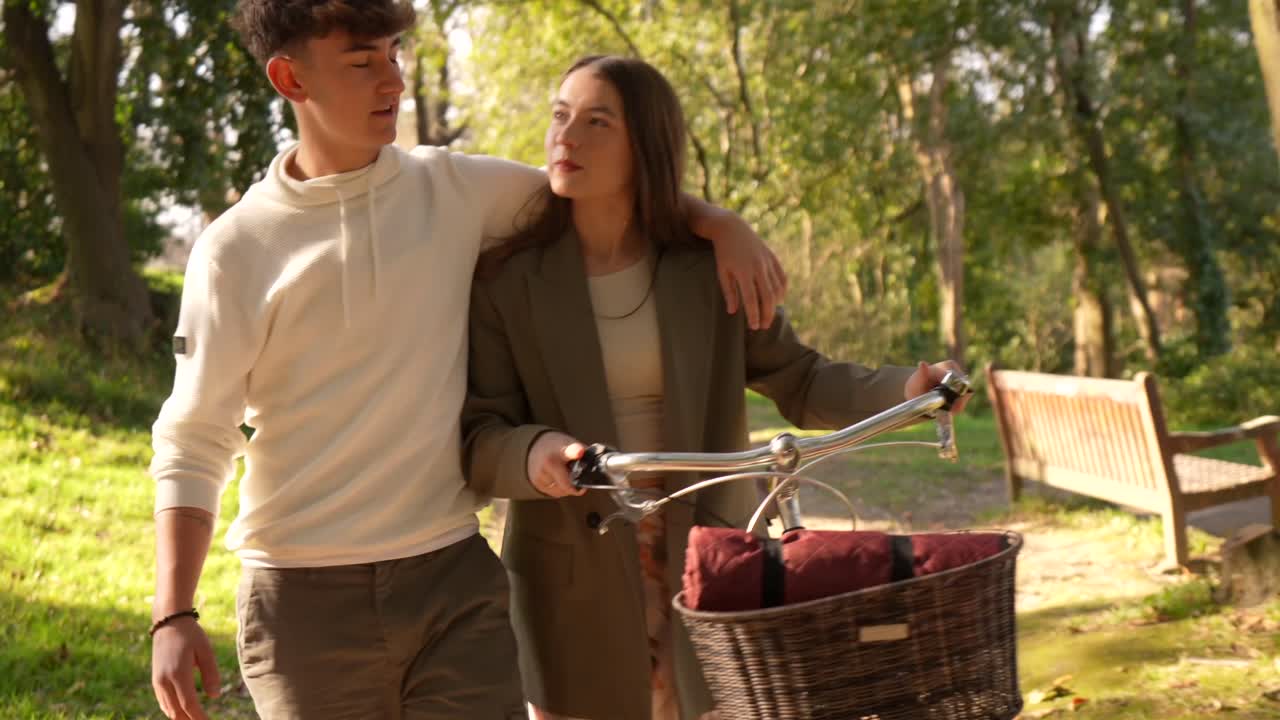 A young couple strolls through the park with a bicycle