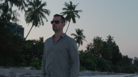 confident man in cool sun glasses walk along tropical beach on the sunset.