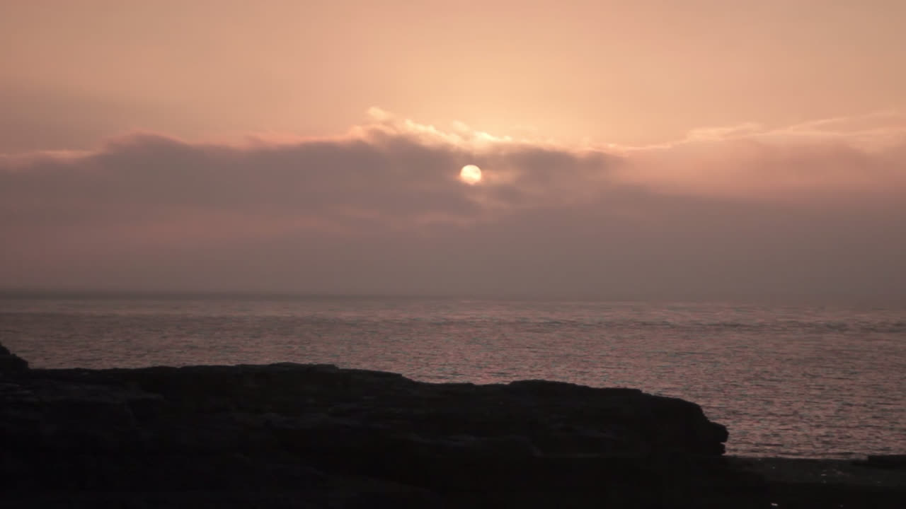 바위에서 바다를 내려다보면 영국 포틀랜드의 청구서에서 바다 위의 하늘에서 떠오르는 태양을 볼 수 있으며 주변에 노란색 색조를 생성합니다.