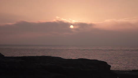 Overlooking-the-sea-from-the-rock-one-can-see-the-sun-rising-from-the-sky-above-the-sea-at-the-bill-in-Portland,-England-and-producing-yellow-hue-in-the-surrounding