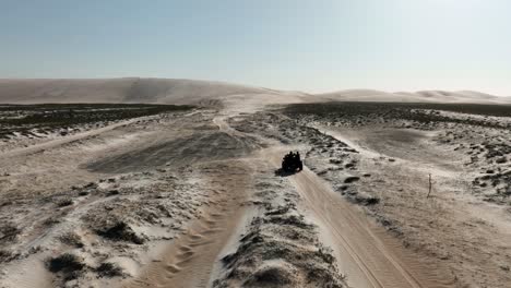 aerial tracking shot of quad bike driving on sandy dunes and northeastern,brazil - desertification during sunny day in dry area