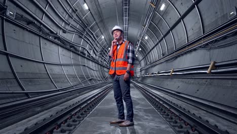 full body side view of asian male engineer with safety helmet thinking and looking around then raising his index finger while standing in underground subway tunnel