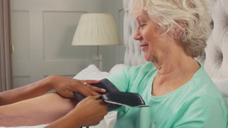 Close-Up-Of-Senior-Woman-At-Home-In-Bed-Having-Blood-Pressure-Taken-By-Female-Care-Worker-In-Uniform