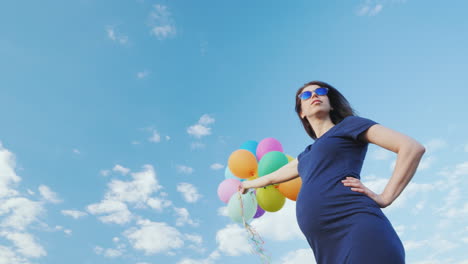 mujer embarazada feliz jugando con globos contra el cielo azul