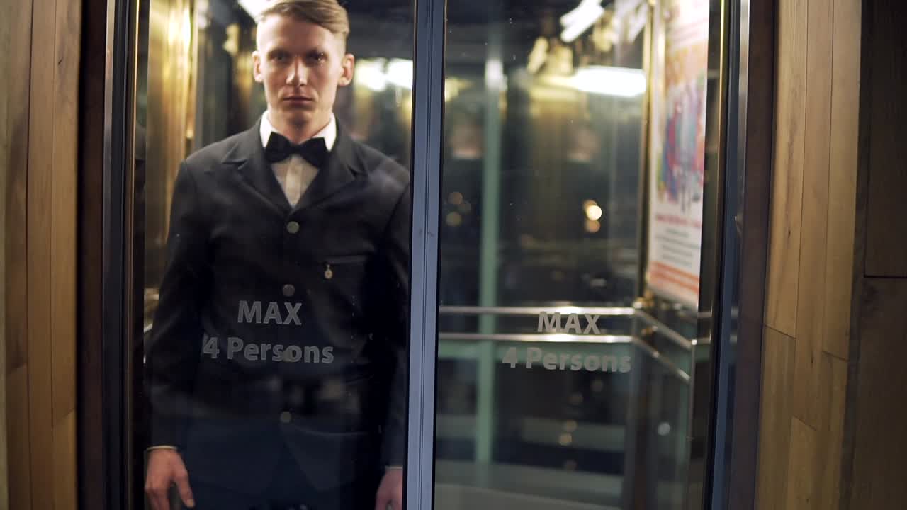 유리 문으로 엘리베이터에서 도착하고 나온  ⁇ 타이를 입은 젊고 성공적인 사업가