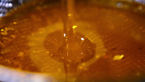 unfiltered freshly extracted honey being poured onto metal sieve. close up. honey filtration after extraction.