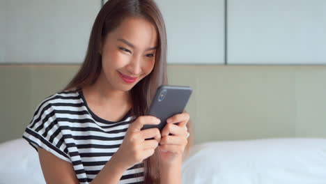 pretty young lady using a mobile phone holding it with her both hands, reading a message and smiling