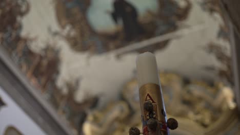 Close-up-of-a-decorated-church-candle-with-an-ornate-ceiling-in-the-background