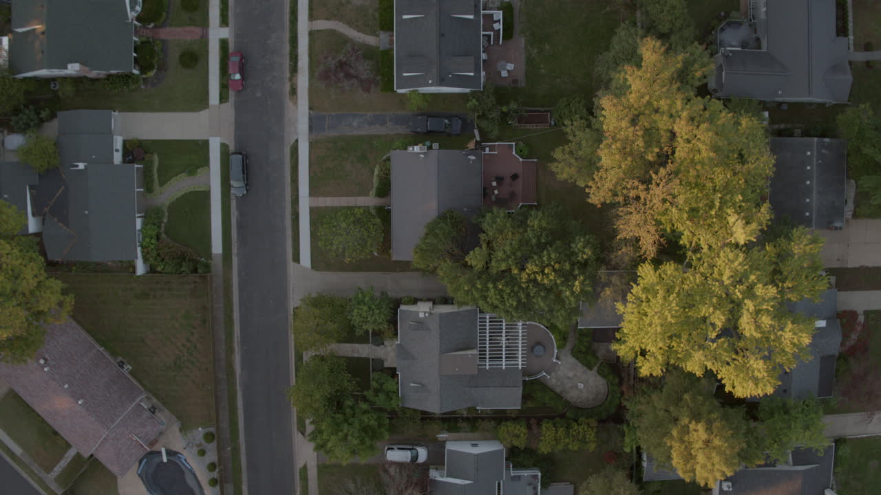 Overhead view of suburban houses, street, trees and driveways camera rises