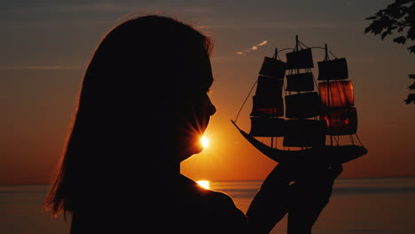 Profil-Einer-Frau-Mit-Einem-Spielzeugsegelboot-Gegen-Die-Untergehende-Sonne
