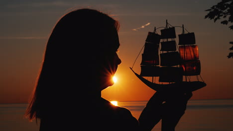 perfil de una mujer con un velero de juguete contra el sol poniente