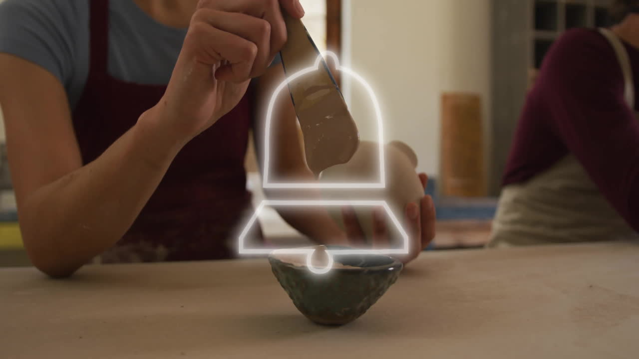 Painting ceramic bowl, person adding glowing bell icon animation in school setting