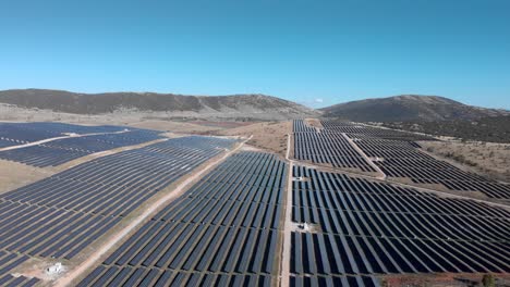 drone ascendente sobre paneles de fila de parque de energía solar fotovoltaica cielo azul todo el día