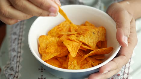 person holding a bowl of tortilla chips and eating one