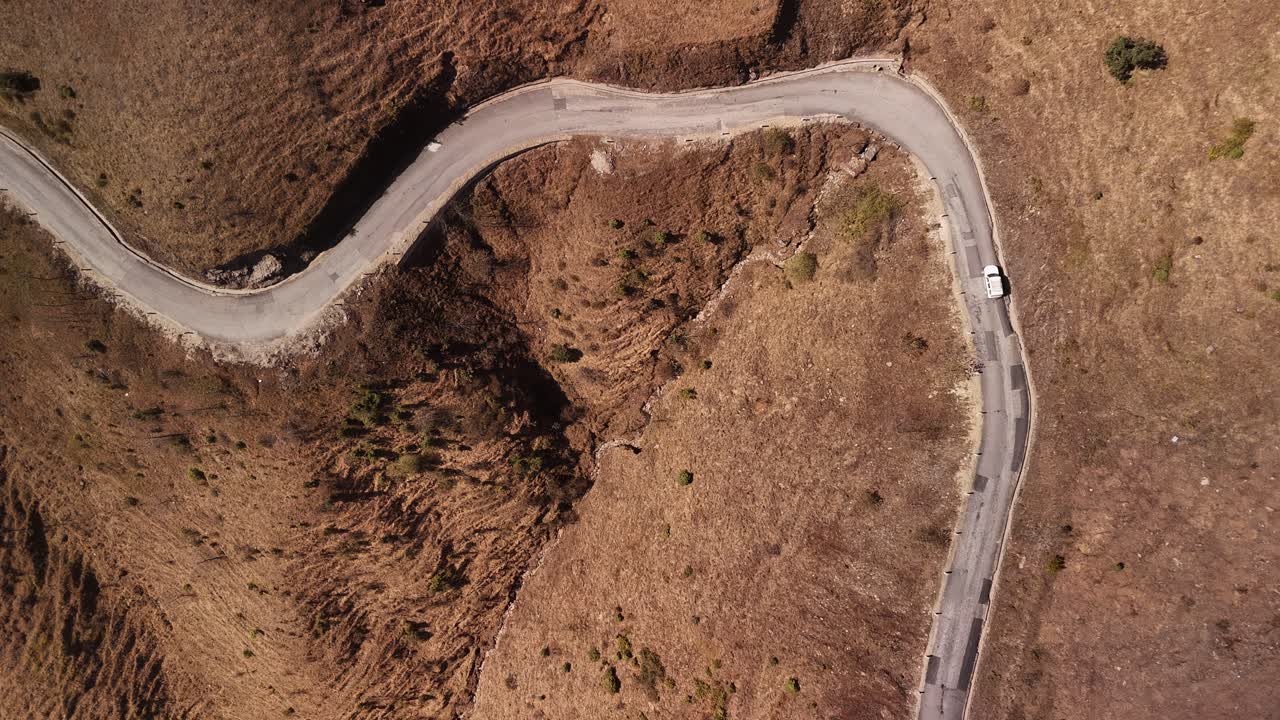 carretera serpenteante a través de un paisaje árido, vista a ojo de pájaros topshot coche blanco viajando a través del paisaje montañoso seco
