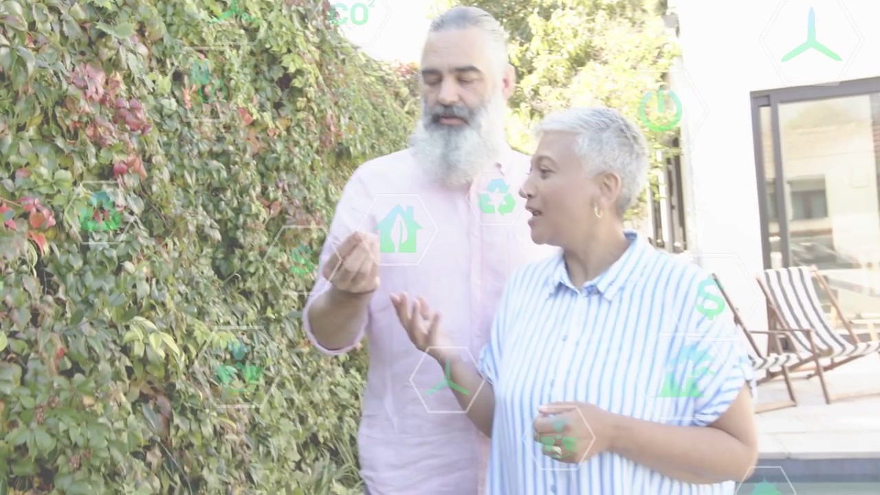 Coppia di giardinieri che passeggia lungo una siepe, la donna indica, l'uomo si allunga per raccogliere una bacca, l'assaggia e ride.