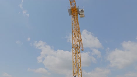 Yellow-tower-crane-on-the-construction-site,-against-blue-sky-with-gently-moving-clouds
