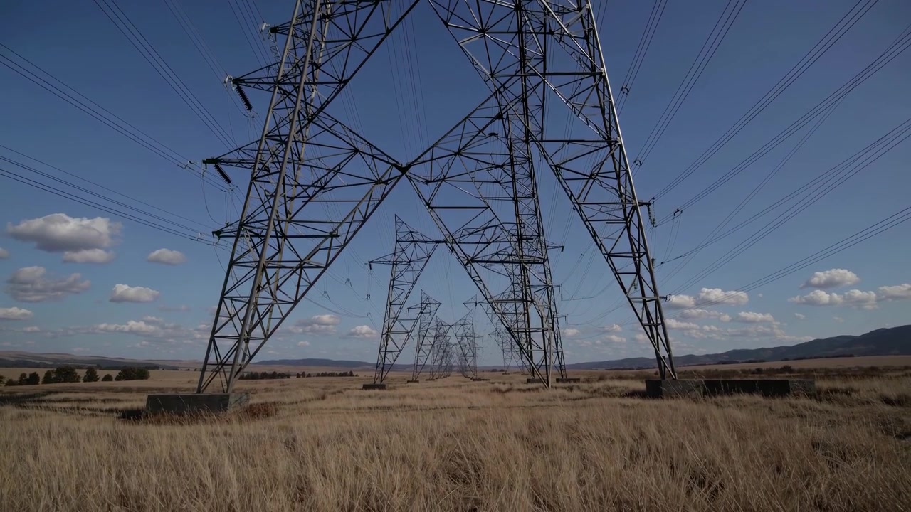 Row of High Voltage Electricity Pylons in a Dry Field