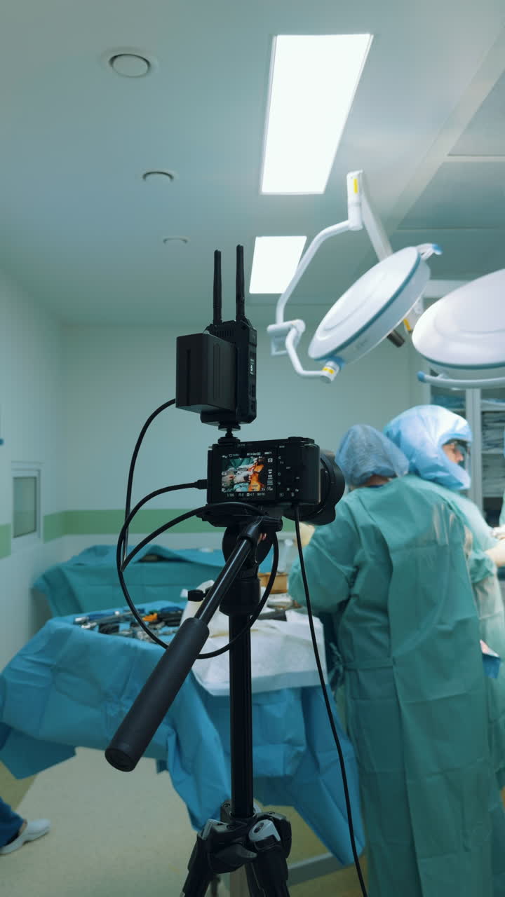 Kyiv, Ukraine, 2 August 2025: Vertical view of a camera setup filming an operation, held by an assistant with focus on the display. The device records the surgical team working blurred in the bright environment