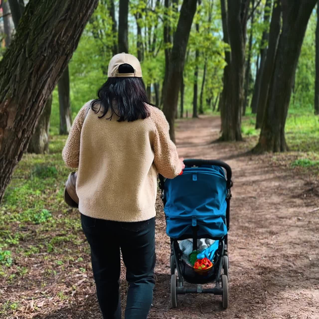 Following the mother with a pram. Woman turns back to the camera. Mom and child go for a walk by the park