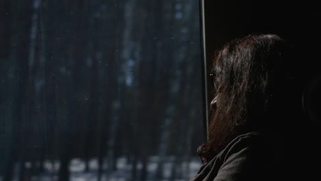 woman gazing out of a train window during a winter journey through snowy finland forests