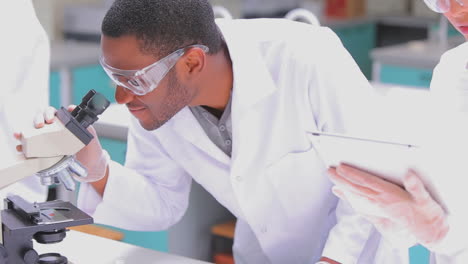 Man-standing-looking-through-the-microscope-with-woman-watching