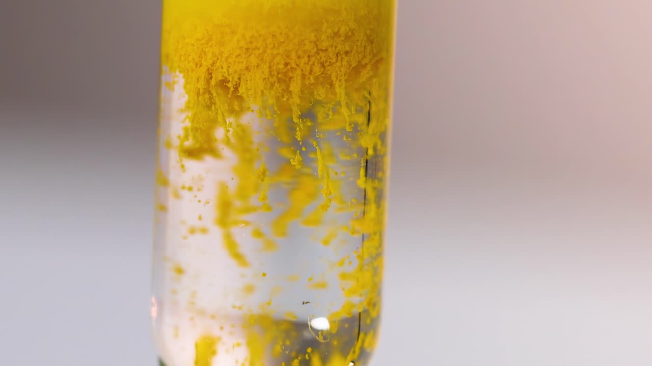 Close-up view of yellow particles forming and settling in a clear liquid within a glass tube.