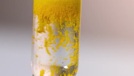 close-up view of yellow particles forming and settling in a clear liquid within a glass tube.