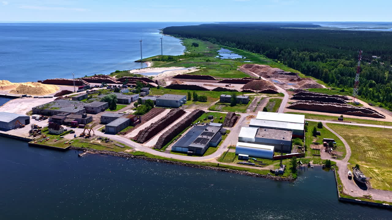 Coastal industrial facility with large log piles and wind turbines at Baltic Sea