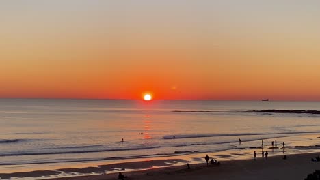 incredible beautiful sunset sky reflections of atlantic ocean waves at carcavelos beach, boats, ships and surfers in the water, orange teal blue tones