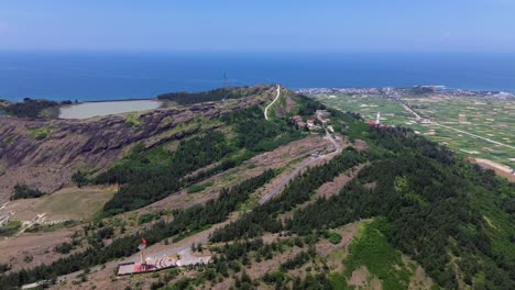 aerial pan right showing geological textures, paths and coastal scenery under intense blue sky