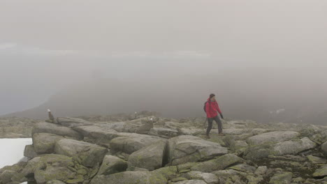 a woman hiking through thick fog on top of a high altitude rocky mountain in norway, slow motion