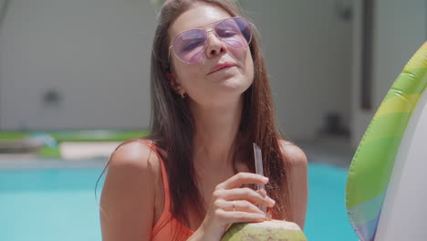 mujer bebiendo agua de coco junto a la piscina