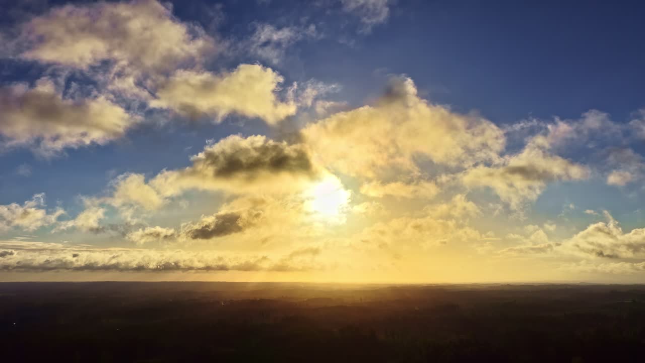 Golden sunlight breaks through drifting clouds during a fast-moving time-lapse over the landscape, capturing dynamic sky movement and atmospheric light