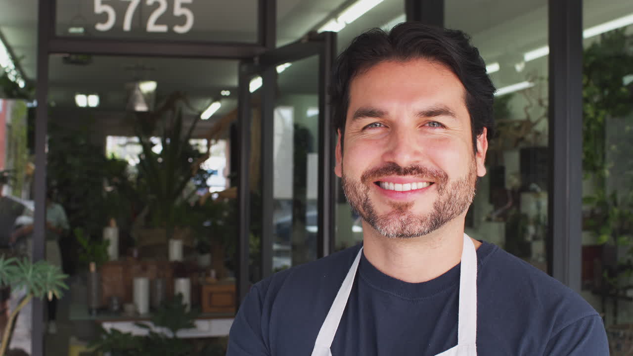 retrato de un dueño de floristería sonriente de pie en la puerta rodeado de plantas
