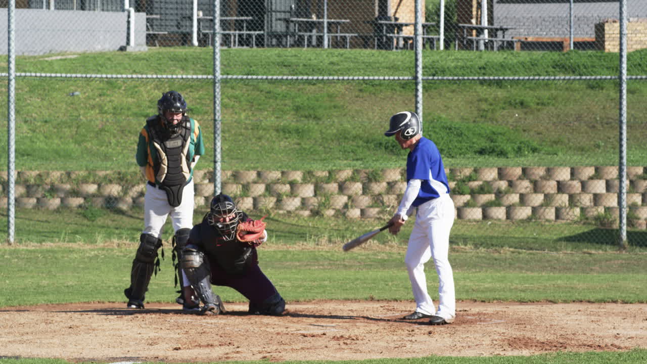 Male baseball players and male umpire playing baseball, catching the ball on a pitch, slow motion