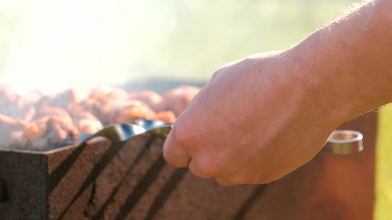 한 남자가 뒷마당의 목탄 그릴 위에 샤슬릭 고기를 요리합니다.