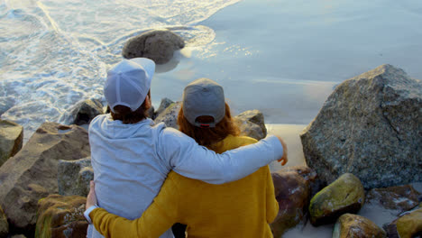 high angle view of young caucasian couple sitting on rock and looking at sea on the beach 4k