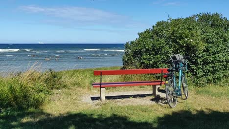 static shot of bike, park bench and green bush by ocean on windy day