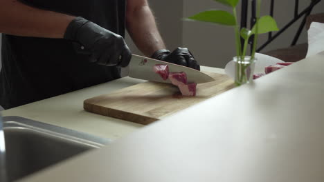 el chef está cortando algunas costillas de cerdo frescas y deshuesadas con un cuchillo afilado y guantes negros protectores