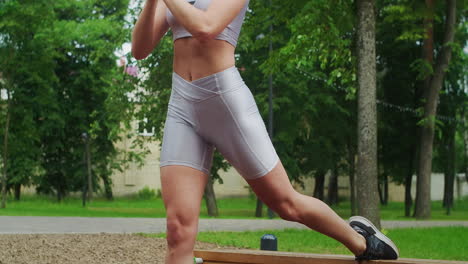 una mujer joven en un parque realiza sentadillas en una pierna en un banco en ropa deportiva en el verano. atletismo mujer caucásica entrena en el parque