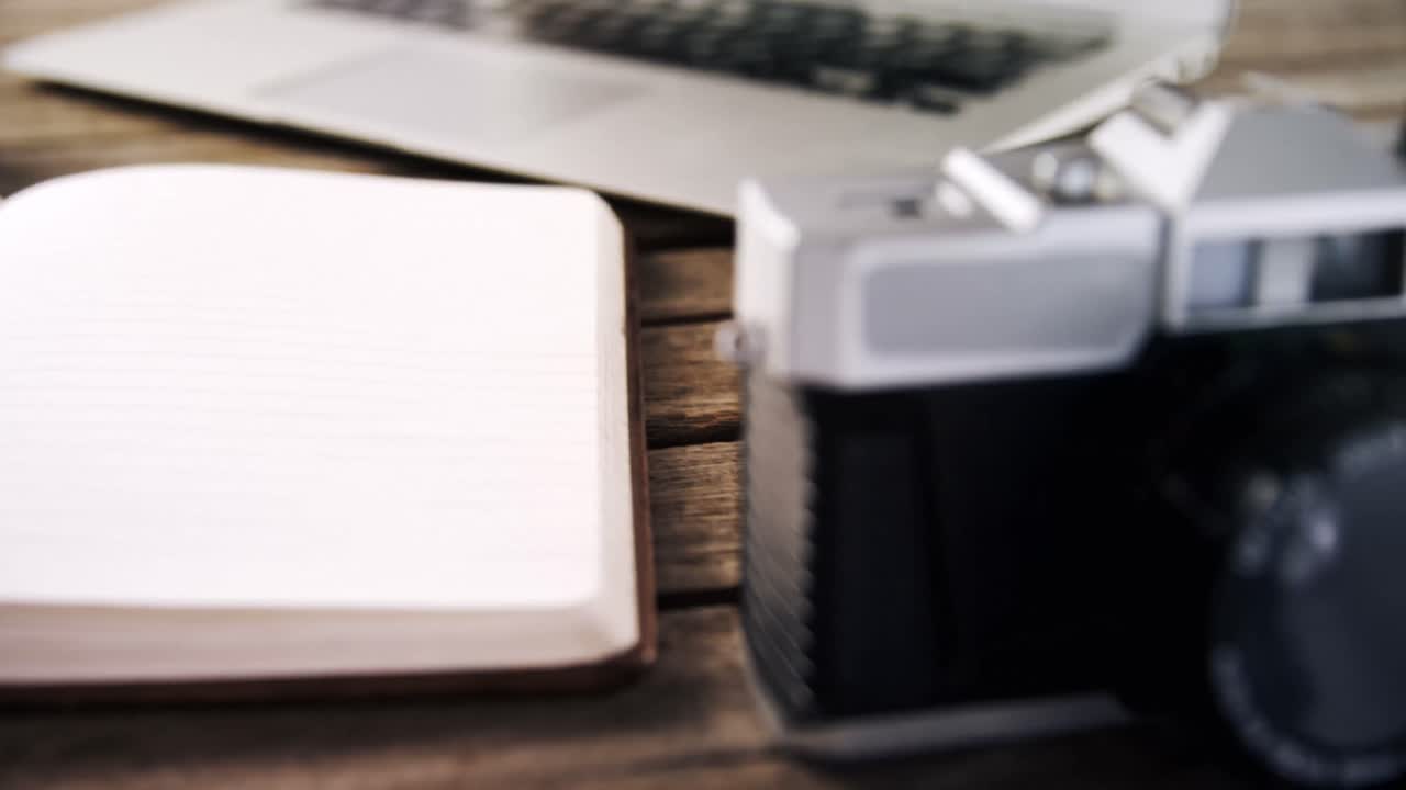 Laptop, diary, and vintage camera on wooden table 4k