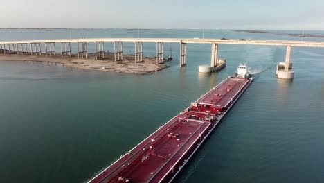 aerial view of a large red barge moving along the gulf intercoastal waterway and under jfk memorial causeway bridge into laguna madre