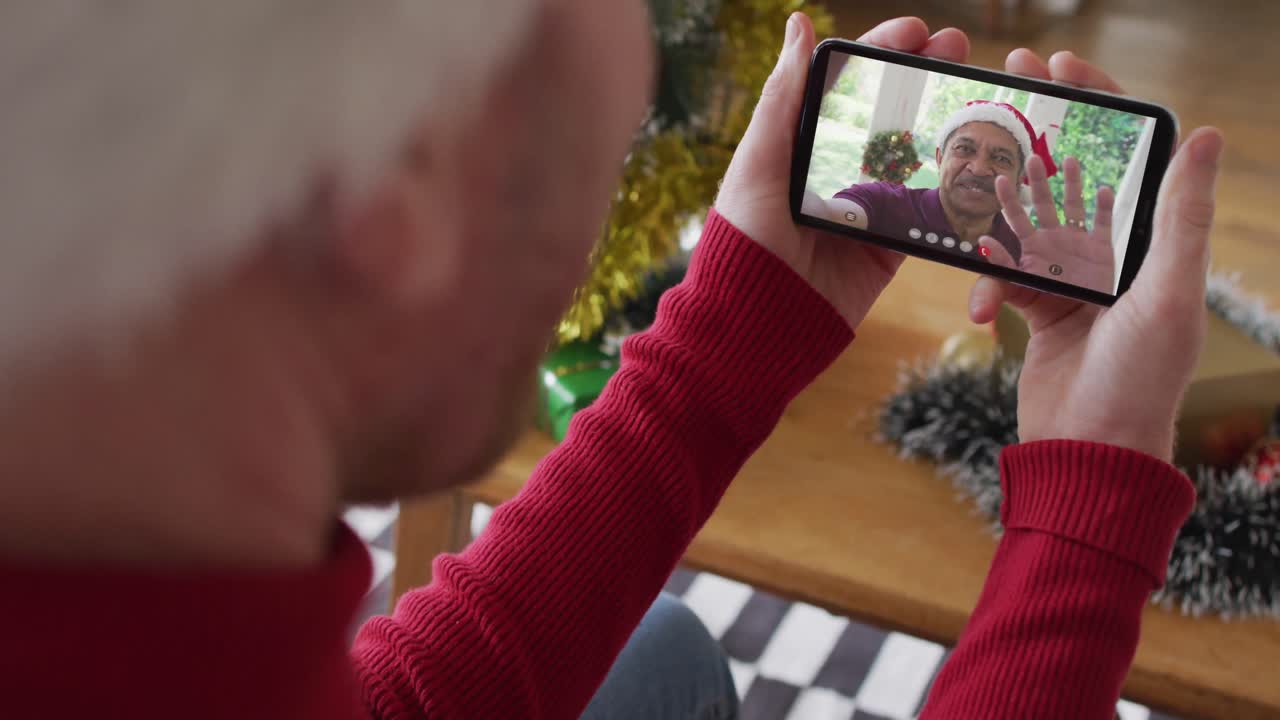 hombre caucásico usando un teléfono inteligente para una videollamada de navidad, con una familia sonriente en la pantalla