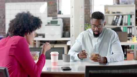 diverse colleagues talking and having lunch at table in office in slow motion