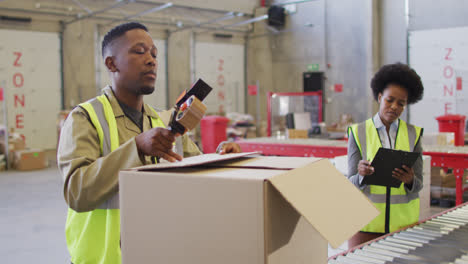 african american male and female workers wearing safety suits and packing boxes in warehouse