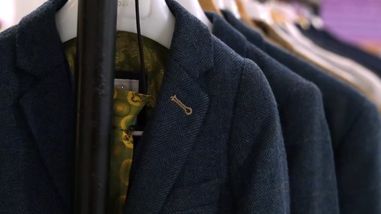 Elegant display of different coloured wedding suits by designer collection. Trendy male fashion essentials on hangers.