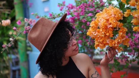 merry hispanic woman smelling and touching flowers