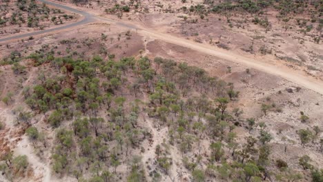 Drohne-Fliegt-über-Raues-Buschland-Im-Australischen-Outback-Und-Erreicht-Eine-Kreuzung-Aus-Asphaltierter-Und-Unbefestigter-Straße